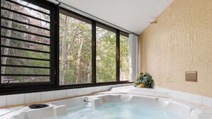 Ett spa-rum med ett bubbelbad, stora fönster och utsikt över träd.