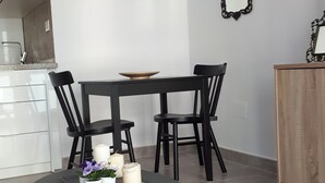 Un comedor con una mesa redonda, sillas negras y mantel negro. En la pared, un cuadro de una escena de playa, un espejo y un aparador de madera.