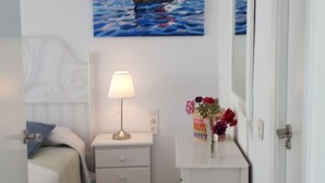 Un dormitorio con cama, mesita de noche, lámpara y un cuadro con barcos en la pared.