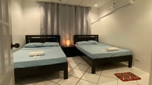 Une petite chambre propre, avec deux lits, une table de chevet, une lampe et un tapis rouge.