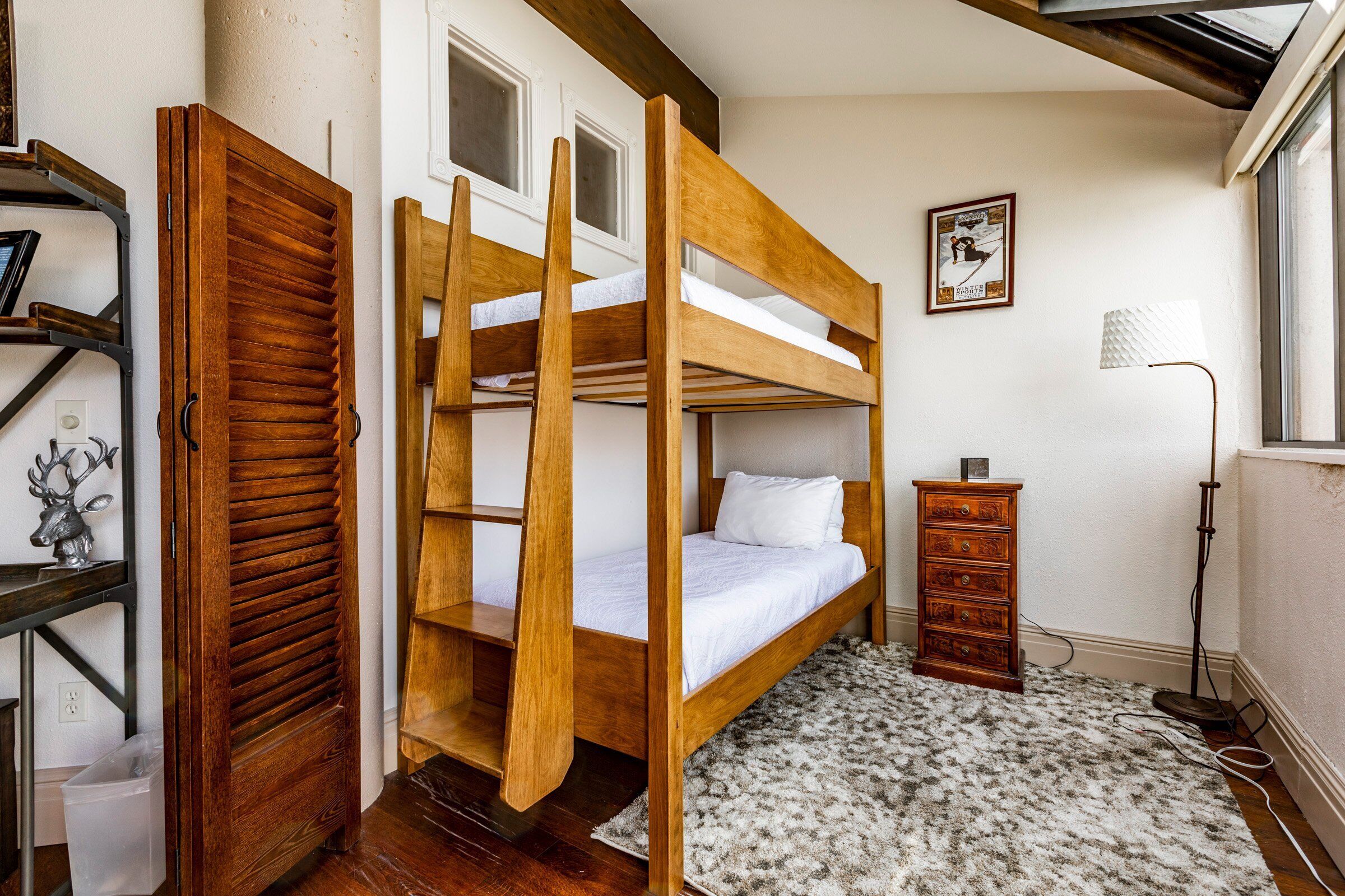 A bunk bed with a wooden frame, a small dresser, a lamp, and a framed picture on the wall.