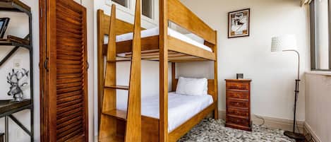 A bunk bed with a wooden frame, a small dresser, a lamp, and a framed picture on the wall.