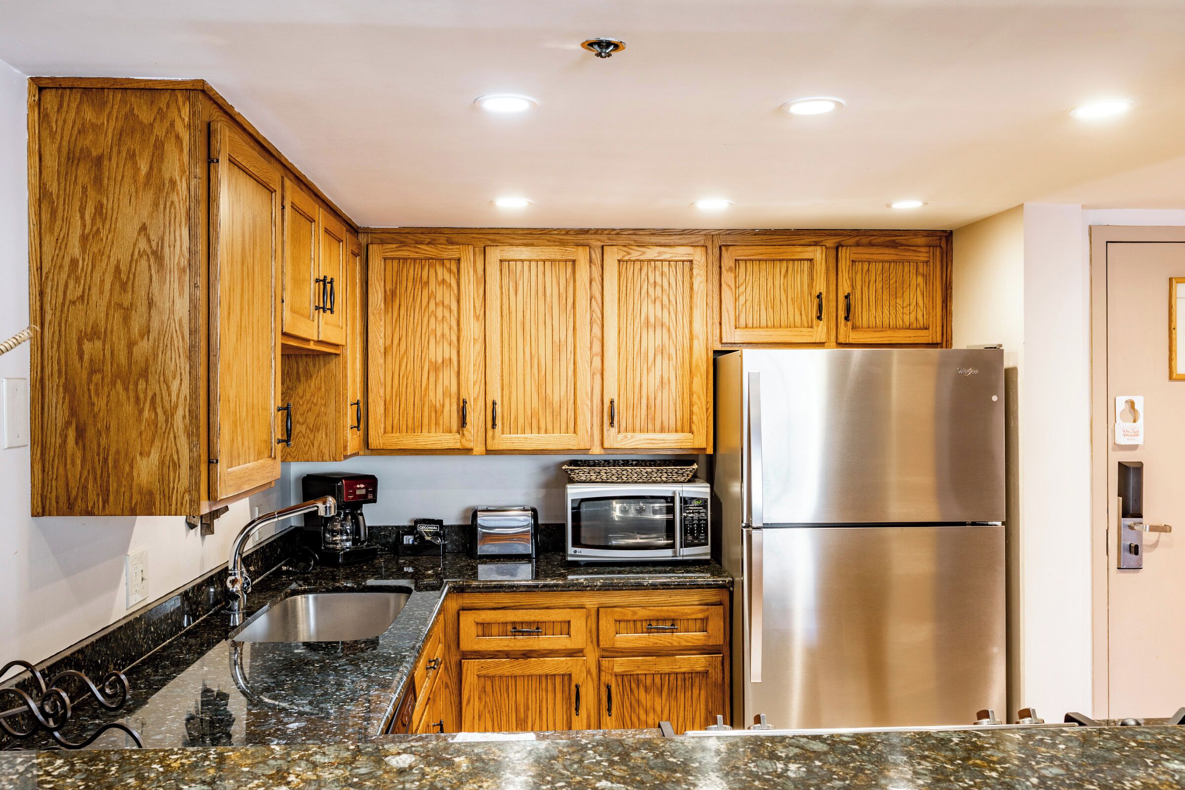 A kitchen with wooden cabinets, a stainless steel refrigerator, a microwave, and a toaster.
