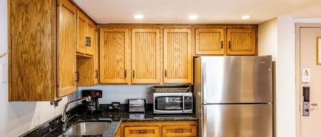 A kitchen with wooden cabinets, a stainless steel refrigerator, a microwave, and a toaster.