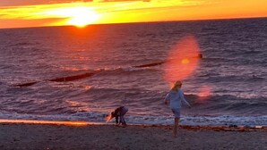 Solnedgang over havet med en strand i forgrunden.