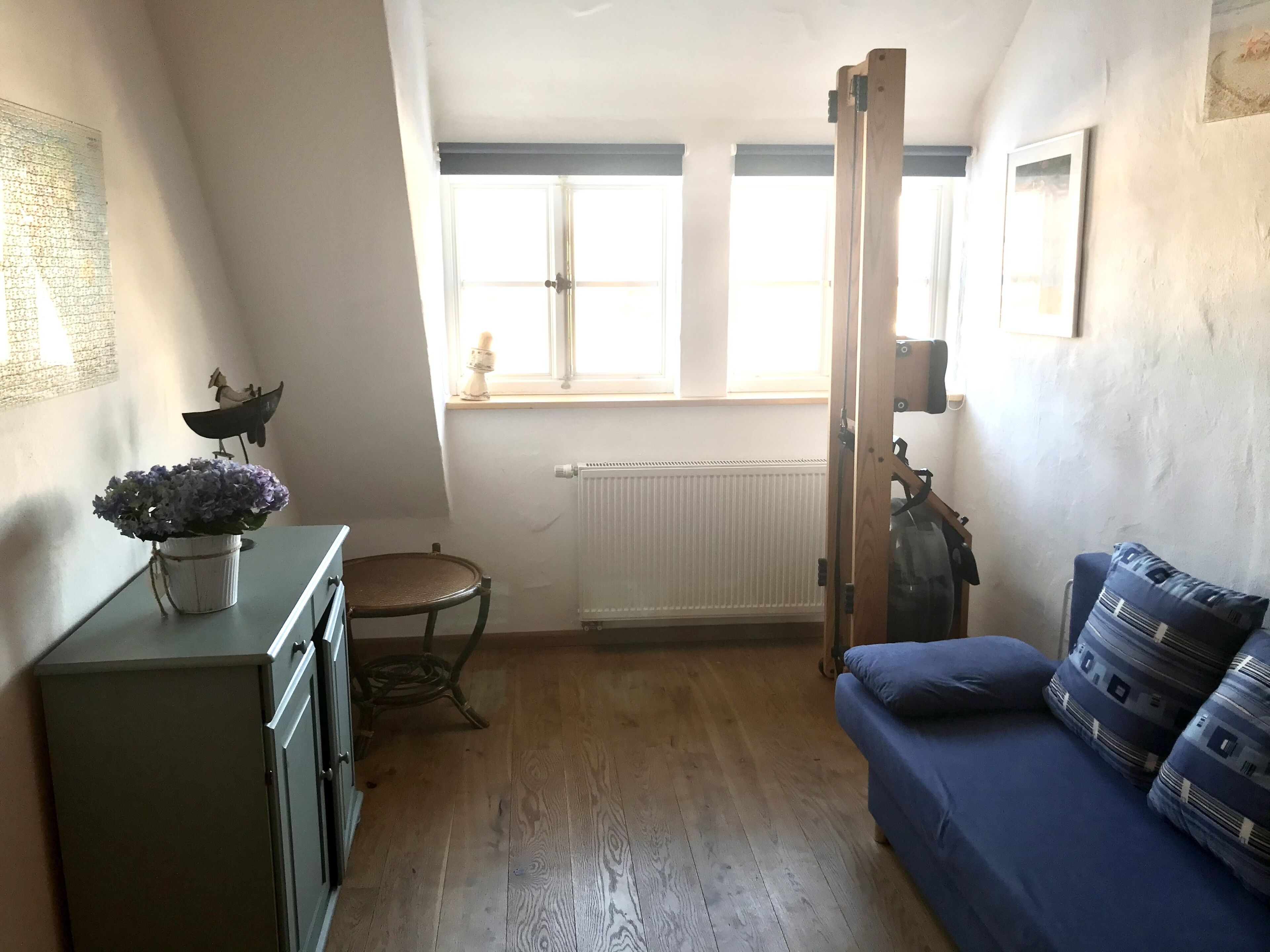 A small, cozy room with a wooden floor, a blue sofa, a green cabinet, and a radiator.