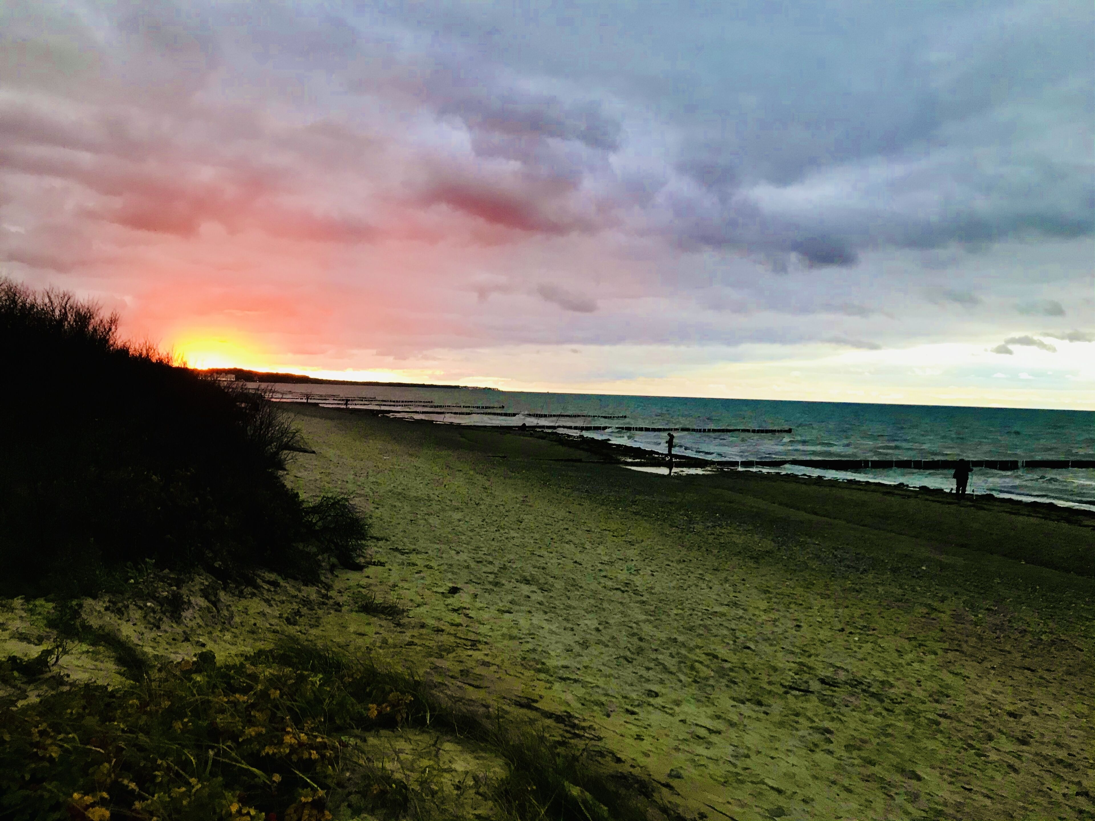 Une plage au coucher du soleil, une jetée et une personne qui se promène.