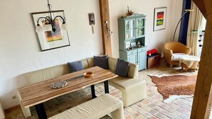 En hyggelig stue med en sofa, et træbord og en bænk. Der er et skab med pynteting og en stol. Rummet har et flisegulv og en stor måtte.