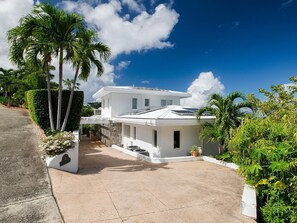 Une maison moderne à deux étages, avec une façade blanche, un patio couvert et une allée menant à l’entrée.