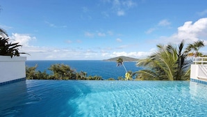 Una piscina infinita de color azul intenso con vistas al océano y una isla distante.