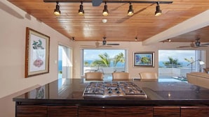 Una cocina moderna con una isla central, techo de madera y grandes ventanales que ofrecen vistas al océano.