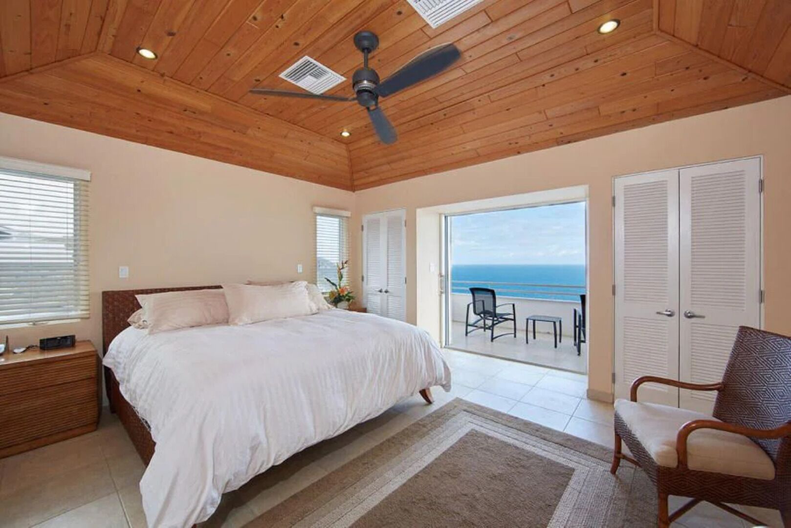 Un dormitorio con una cama grande, ventilador de techo y vista al océano a través de una puerta corredera.