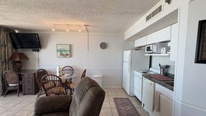 A compact living space with a kitchenette, a dining area with chairs, a sofa, and a television mounted on the wall. - Oceanfront Condo in Myrtle Beach  (Myrtle Beach)