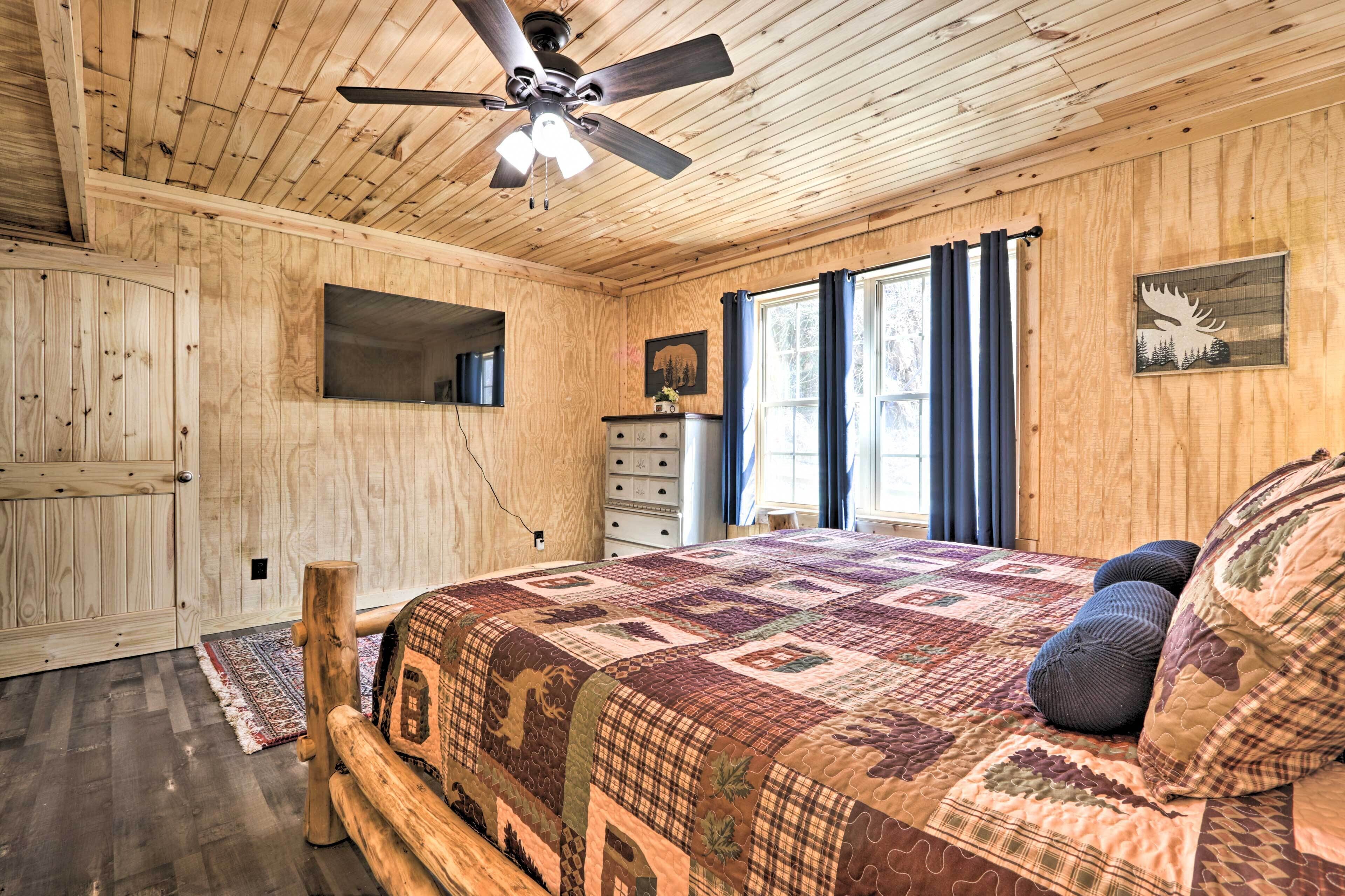 A wooden cabin bedroom with a bed, a ceiling fan, a dresser, and a window with curtains.