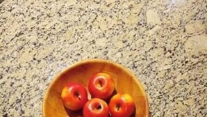 Un tazón de madera con seis manzanas sobre una encimera de granito.