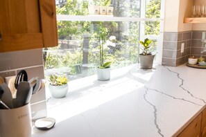 Keittiössä on valkoisesta marmorista valmistettu työtaso, ruukkukasveja ja ikkuna, josta avautuu näkymä vehreään maisemaan.