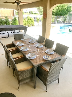 Un patio al aire libre con una mesa de madera dispuesta para seis personas, rodeado de sillas de mimbre con cojines.