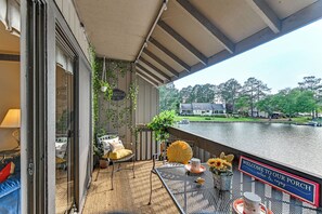 Un balcon donnant sur un lac, une table sur laquelle est posée une pancarte indiquant « Bienvenue sur notre véranda », et une chaise avec un coussin jaune.