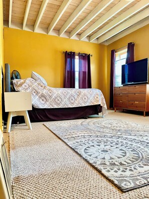 Une chambre à coucher avec un lit, une télévision, une commode et une fenêtre avec des rideaux.