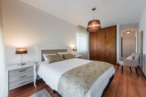 Camera da letto moderna con un letto grande, due comodini con lampade, un armadio in legno, una sedia e un lampadario.