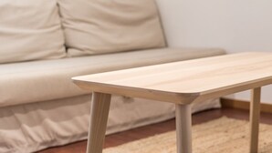 Ein schlichter Holztisch mit heller Oberfläche, platziert vor einem beige gefärbten Sofa mit passender Kissenlehne.