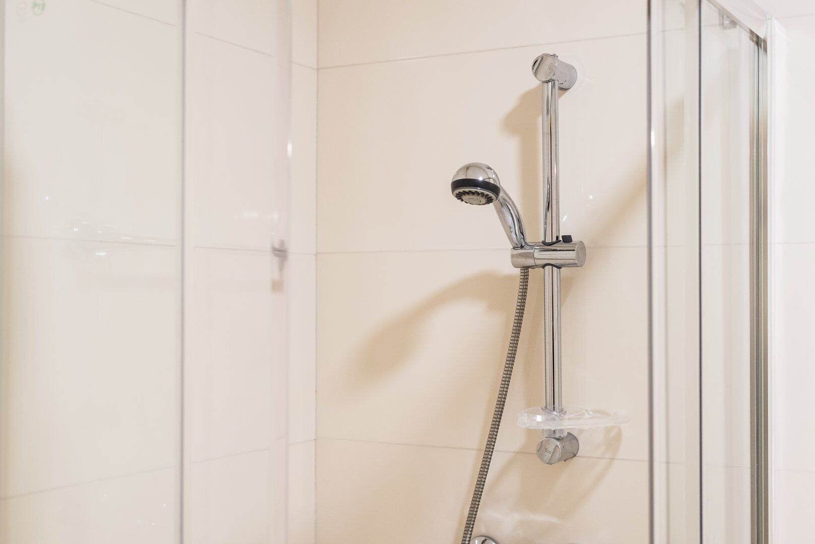 A shower with a handheld showerhead and a fixed showerhead, both mounted on a wall.