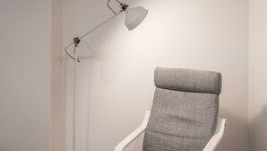 Ein Sessel mit grauem Stoffbezug und einer weißen Armlehne, neben einer weißen Stehlampe mit metallischem Fuß und weißem Lampenschirm.