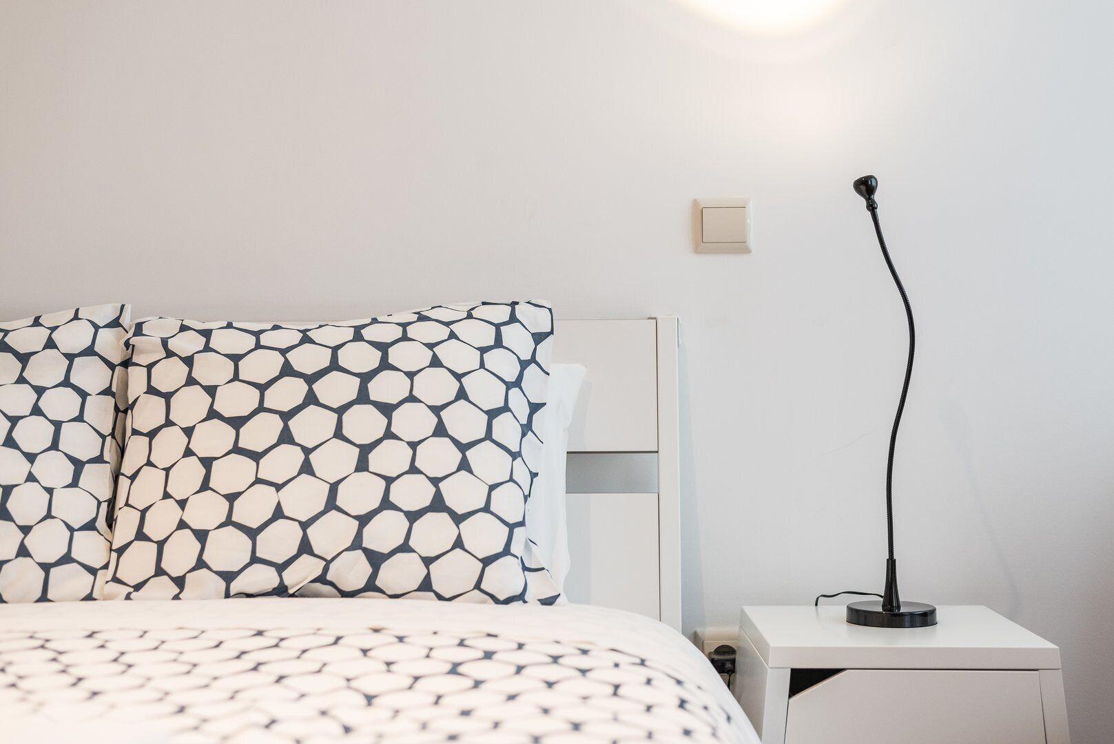 Un lit bien fait, avec une literie à motifs, une table de chevet avec une lampe et un luminaire fixé au mur.