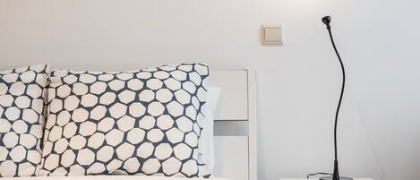 Un lit bien fait, avec une literie à motifs, une table de chevet avec une lampe et un luminaire fixé au mur.