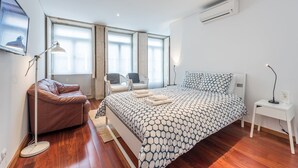 Een moderne slaapkamer met een groot bed, twee stoelen, een bureau en een staande lamp.