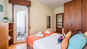 Une chambre à coucher comprenant un lit, une armoire, une porte donnant sur un balcon et une petite table avec une plante.
