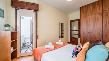 Un dormitorio con cama, armario, puerta que da a un balcón y una mesita con una planta.
