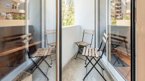 Un balcon avec deux chaises en bois et une petite table, entouré de murs en verre.