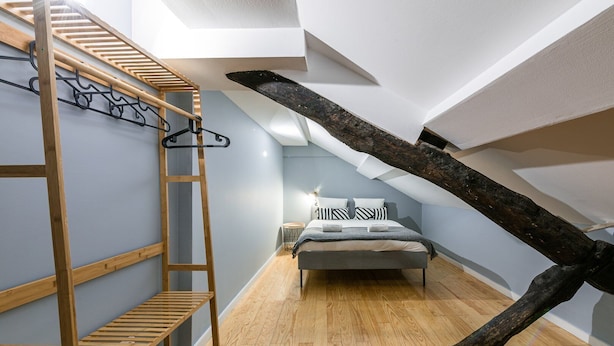 A loft bedroom with a wooden ladder, a bed with striped bedding, and a large tree branch as a ceiling feature. - GuestReady - Miragaia Rooftop (Porto)