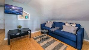 A modern living room with a blue sofa, a black coffee table, and a TV mounted on the wall. - GuestReady - Miragaia Rooftop (Porto)