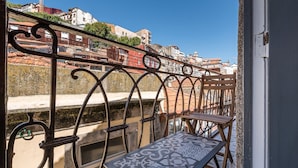 A balcony with a metal railing, a small table with a patterned tablecloth, and a view of buildings in the background. - GuestReady - Miragaia Rooftop (Porto)
