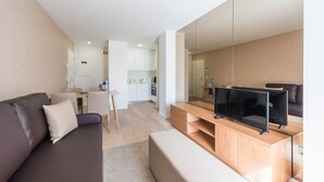A modern living room with a sofa, a TV on a wooden stand, and a kitchen in the background. - GuestReady - Mushroom (Porto)