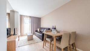 A modern living room with a sofa, a dining table with chairs, a small desk with a computer, and a window with curtains. - GuestReady - Mushroom (Porto)