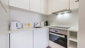 A compact kitchen with white cabinets, a built-in oven, a coffee maker, and a kettle. - GuestReady - Mushroom (Porto)