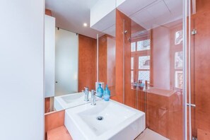 Un baño moderno con un lavamanos blanco grande, un espejo y una cabina de ducha con paredes de vidrio.