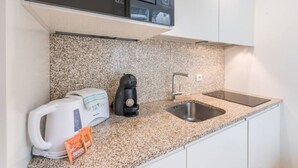 A kitchen with a granite countertop, a kettle, a coffee maker, and a sink.