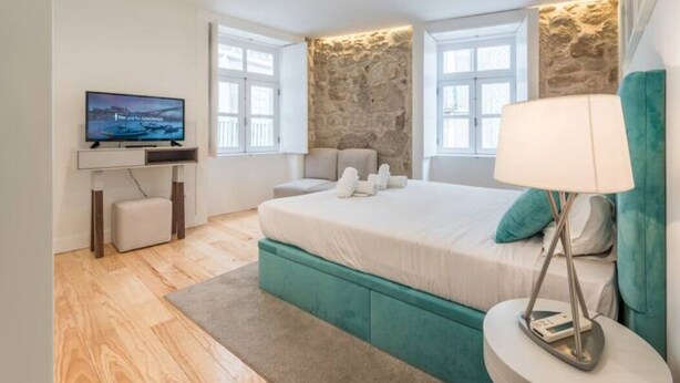 A modern bedroom with a large bed, a television, and a stone accent wall.