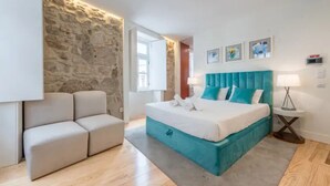 A modern bedroom with a stone accent wall, a large bed with teal bedding, a white sofa, and a small bedside table.
