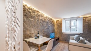 A cozy room with a stone wall, a white table with two chairs, a TV, and a sofa with cushions.
