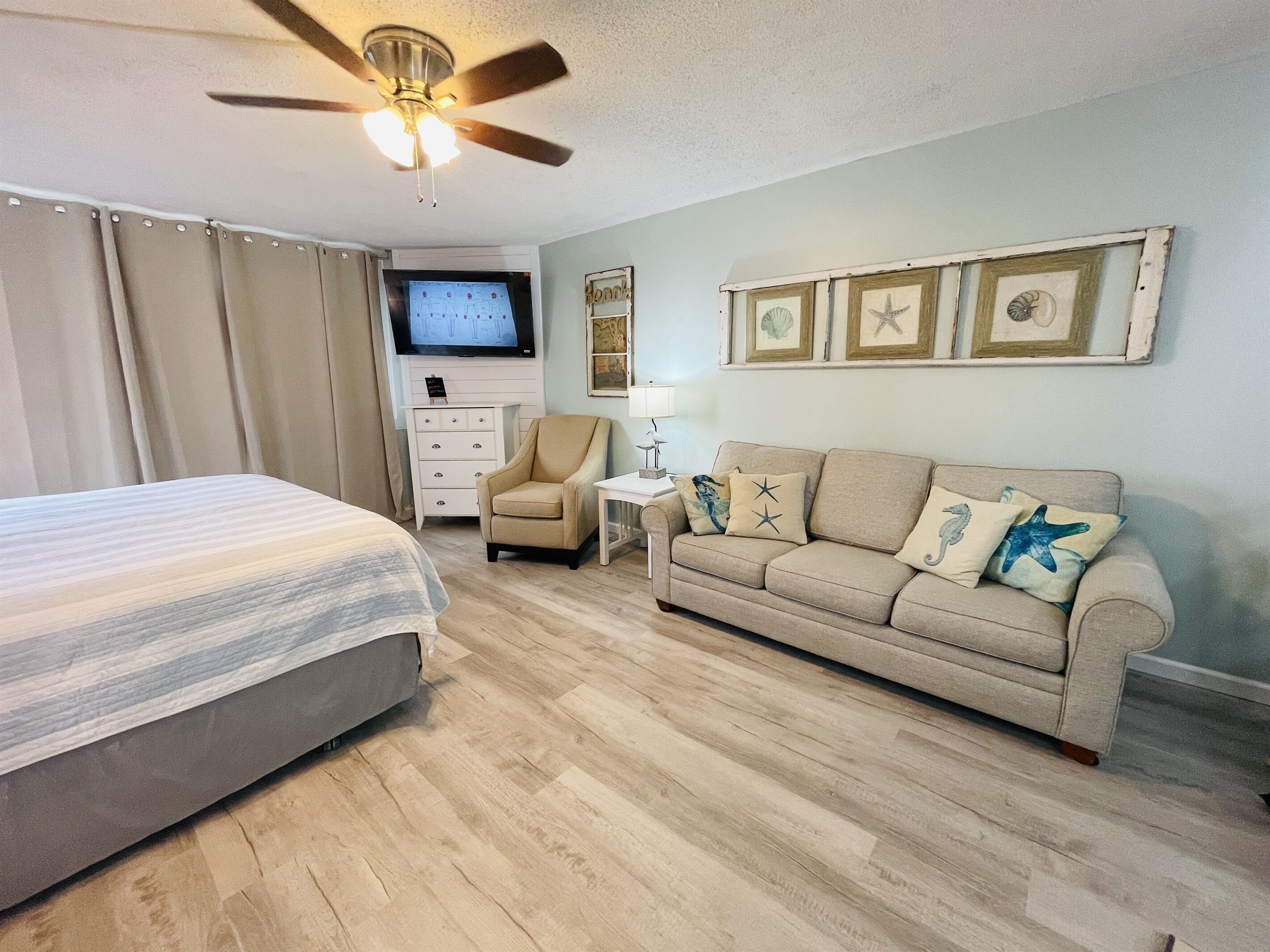 A hotel room with a bed, a sofa, a chair, a TV, and framed pictures on the wall.