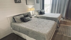 A bedroom with two beds, a star decoration, motivational wall art, a lamp, and a view of the outdoors. - Chill Beach front complex Two Queens at Top of the Gulf (Panama City Beach)