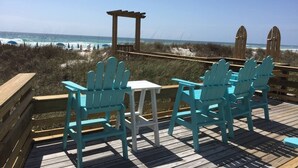 A wooden deck with turquoise Adirondack chairs and a small white table, overlooking the beach and ocean. - Chill Beach front complex Two Queens at Top of the Gulf (Panama City Beach)