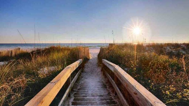 A wooden boardwalk leading to a beach with the sun setting in the background. - Chill Beach front complex Two Queens at Top of the Gulf (Panama City Beach)