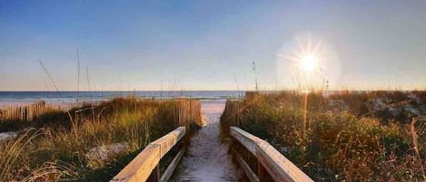 A wooden boardwalk leading to a beach with the sun setting in the background.