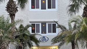 Una entrada de hotel con un camino bordeado de palmeras que conduce a un acceso con puertas dobles.